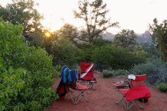 3 chairs on Sedona red earth surrounded by green shrubs. This represents the feeling of doing a Sedona outdoor seminar or circle.