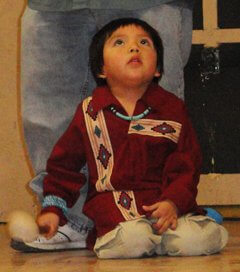 Hopi child holding drum stick and keeping rhythm with his family who is performing a song. This represents the raft attention of a child and learning by observing.