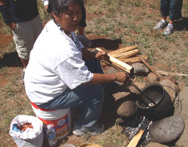 Hopi woman is stirring corn kernels in kettle over open fire making traditional parched corn.