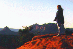Woman standing on red cliff at sunset in deep solo meditation with nature. Symbolizes connecting with the natural life forces in solo communion with nature.