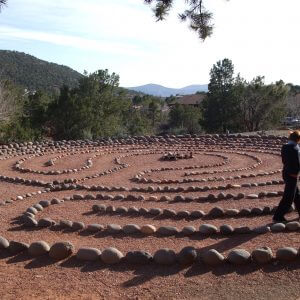 Large 11-path labyrinth with person walking it represents a group ceremony site used by Crossing Worlds Journeys.