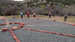 Large medicine wheel with stone spokes and blue gravel base with people standing on rim symbolizes personalized Sedona ceremonial training done by Crossing Worlds at this private site.
