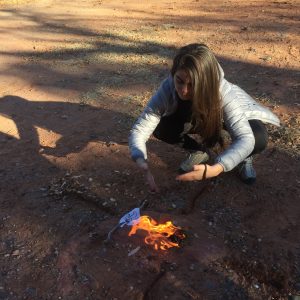 Photo of a woman kneeling with her hands above a small fire. This symbolizes the use of ceremony during a Sedona spiritual retreat to activate positive change..