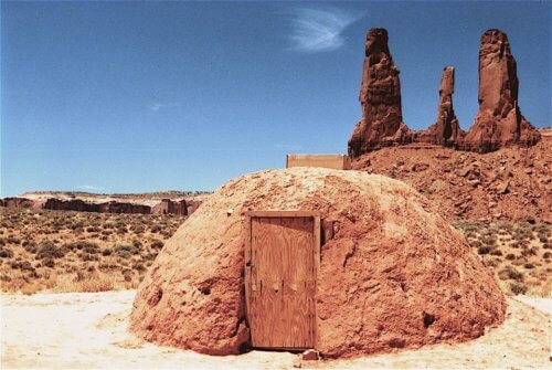 Navajo hogan with 3 red rock spires behind it speak of Navajo people being at home out on the wide open landscapes of the Colorado Plateau