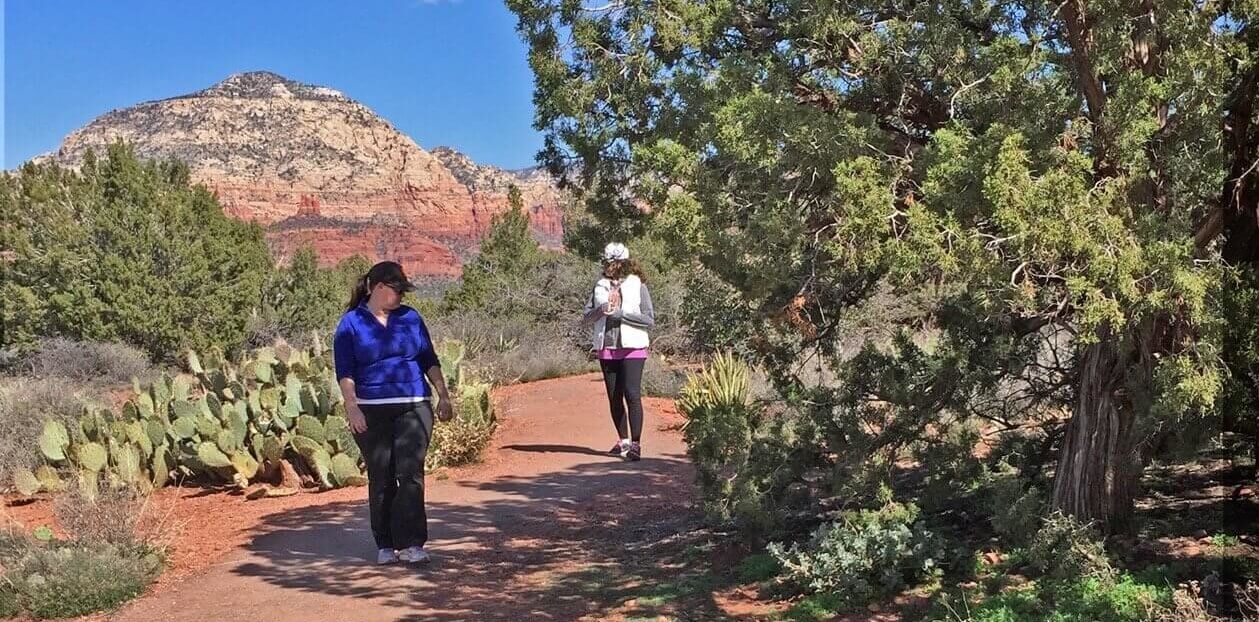 2 people walking slowly on a red earth path with Thunder Mountain in background. They are doing deep observing in nature.